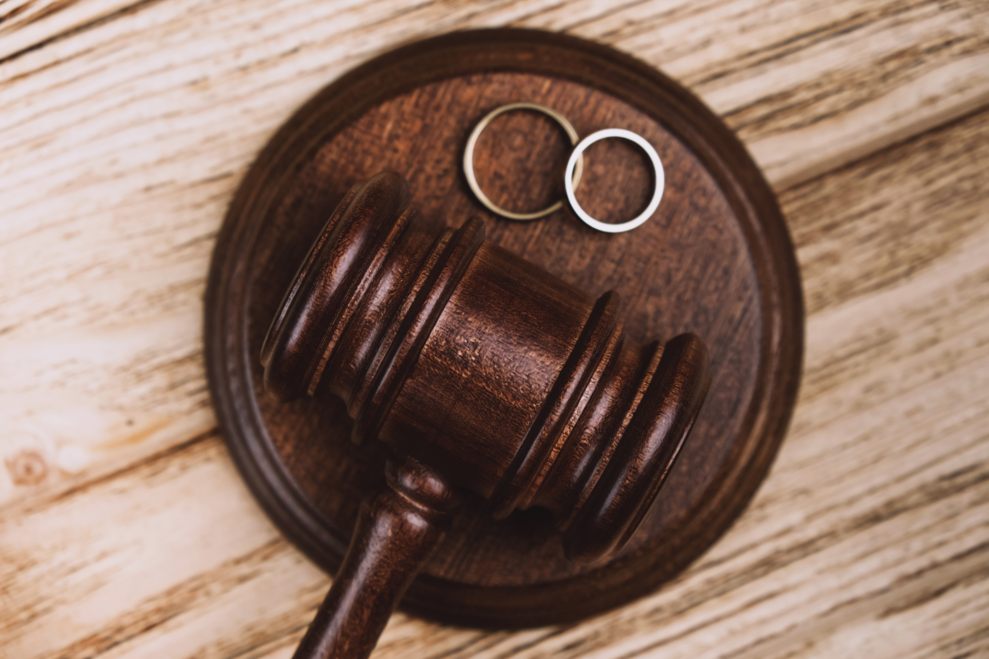 A judge's gavel on a wooden surface, with two wedding rings placed beside it, symbolizing divorce or legal separation