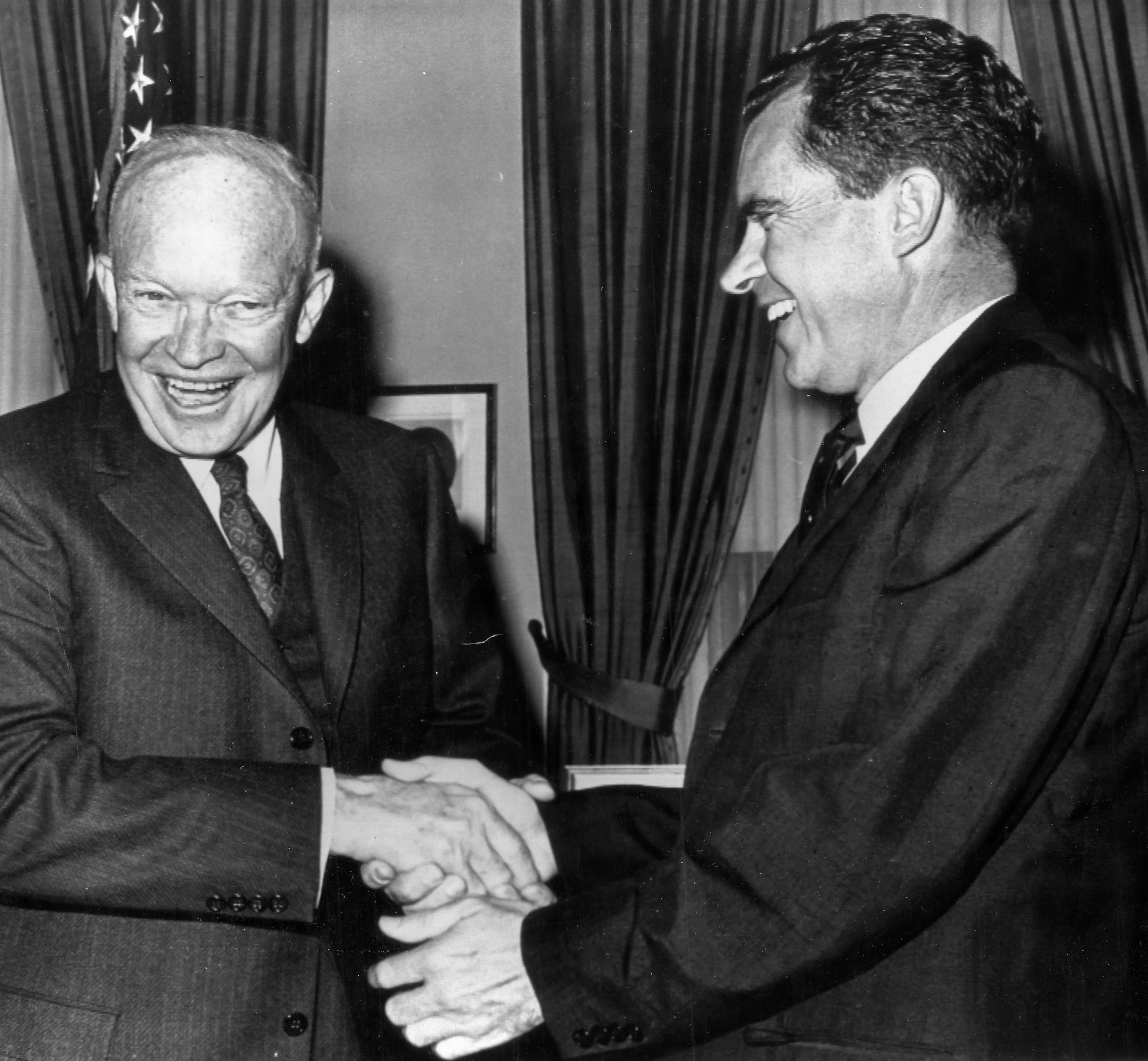 Dwight D. Eisenhower and Richard Nixon smiling and shaking hands in a formal setting, both wearing suits