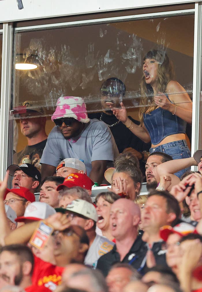 I don’t know who the people in the image are. One person wears a pink bucket hat, another person wears a dark hat, and a third person in a denim outfit is cheering