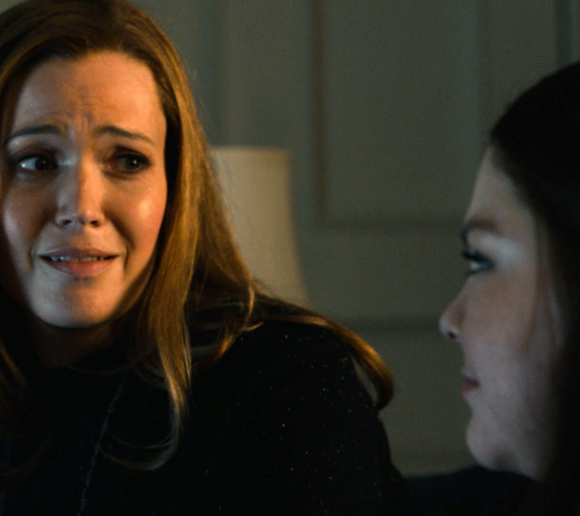 Two women, sitting close together indoors, appear to be having an emotional conversation. Faces are slightly illuminated, showcasing their expressions