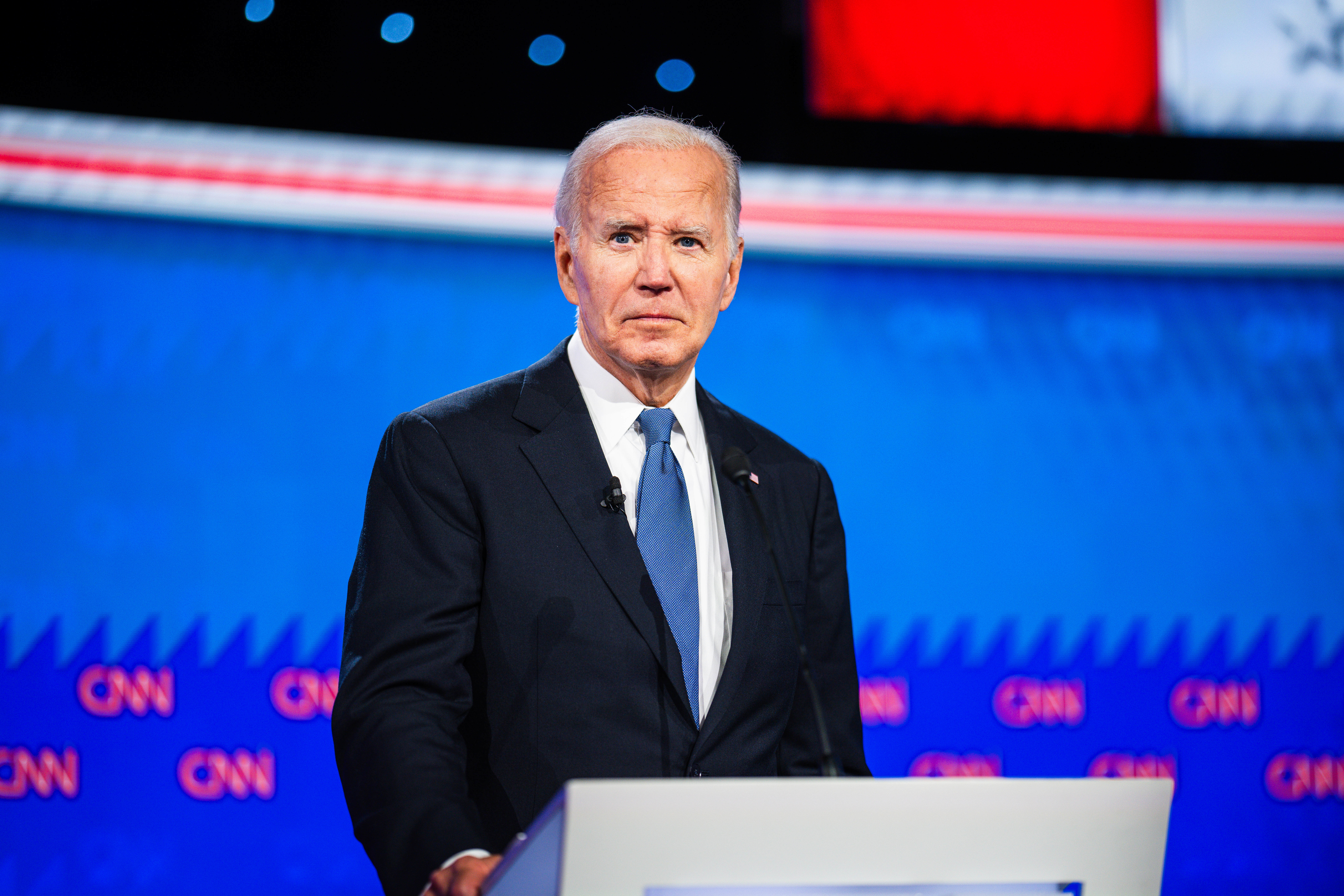 Joe Biden stands behind a podium during a CNN event, dressed in a formal suit and tie, on a blue-themed stage