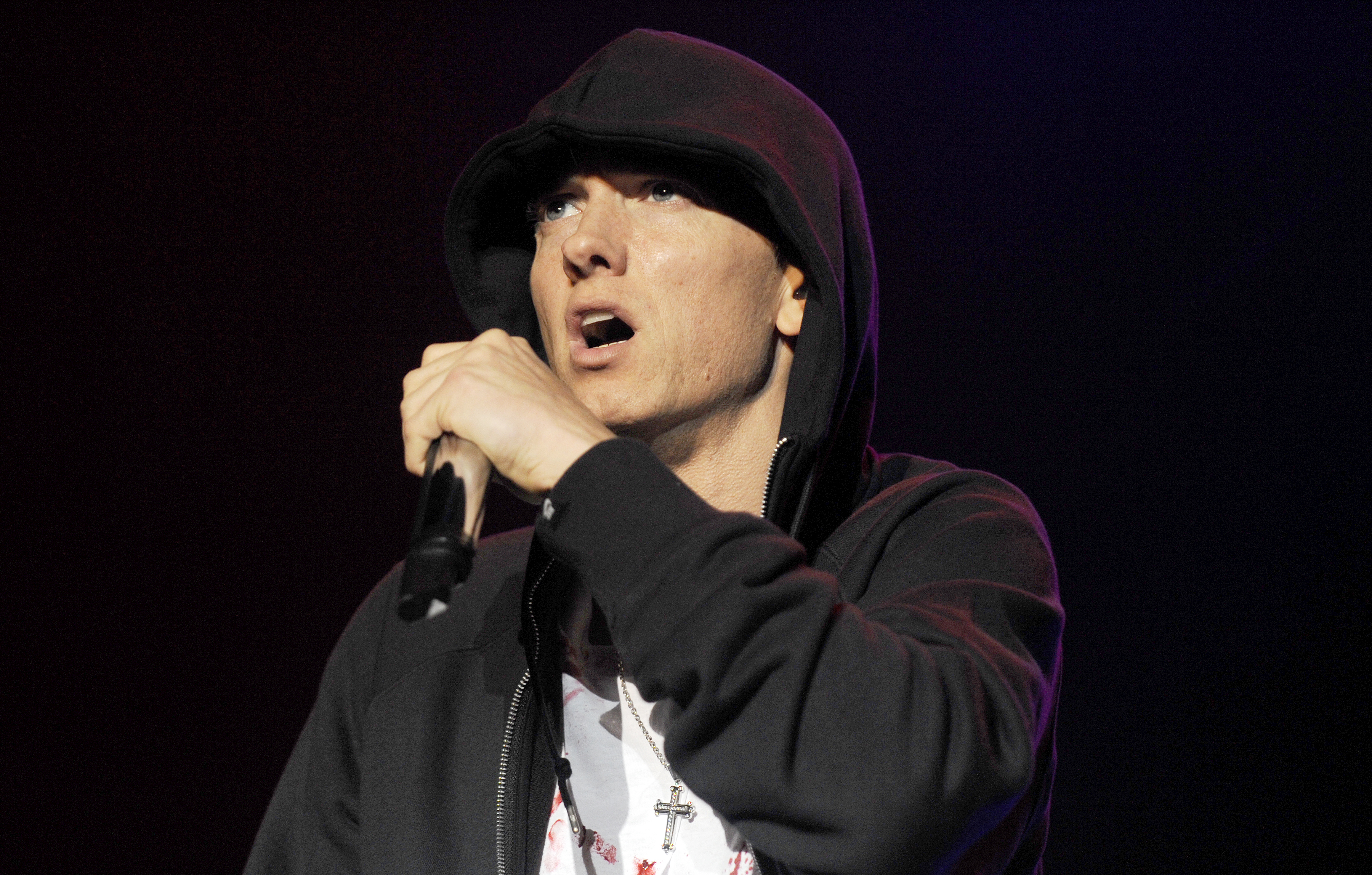 Eminem is performing on stage, wearing a hoodie and holding a microphone