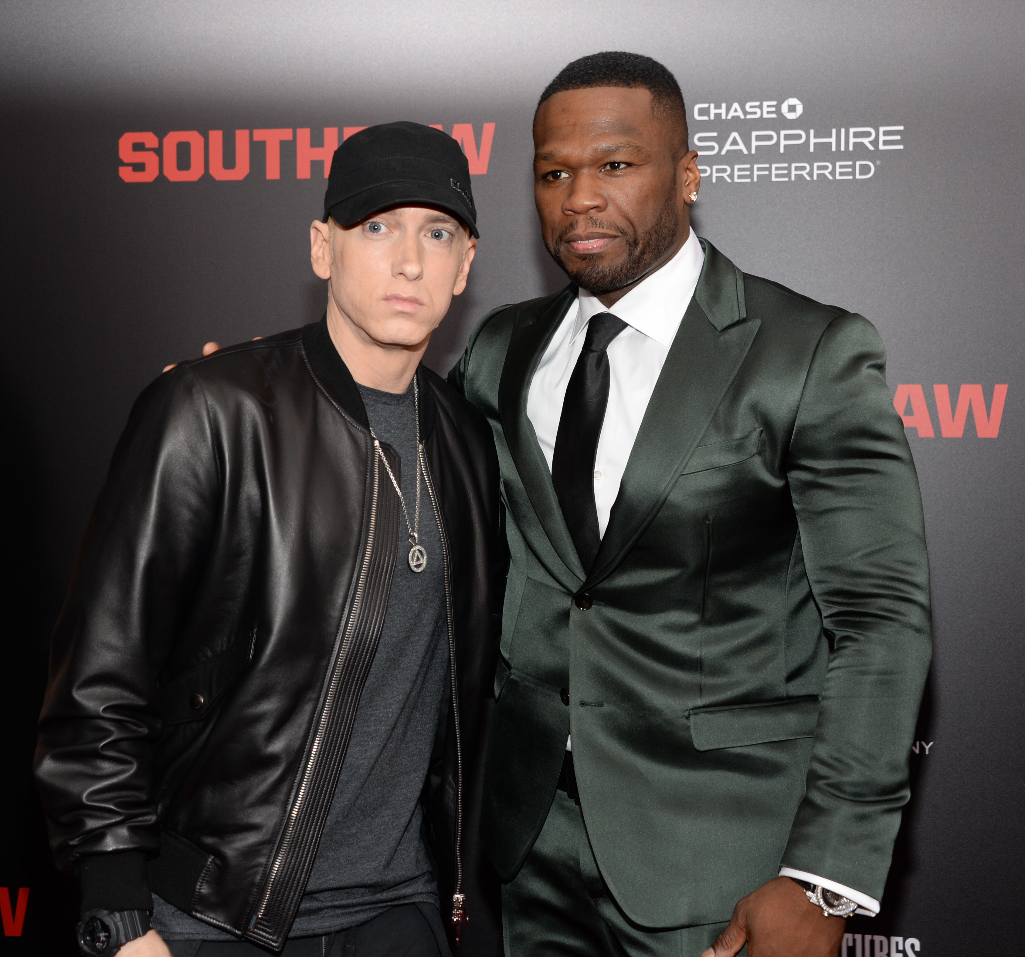 Eminem in a black jacket and cap next to 50 Cent in a green suit at a &quot;Southpaw&quot; event