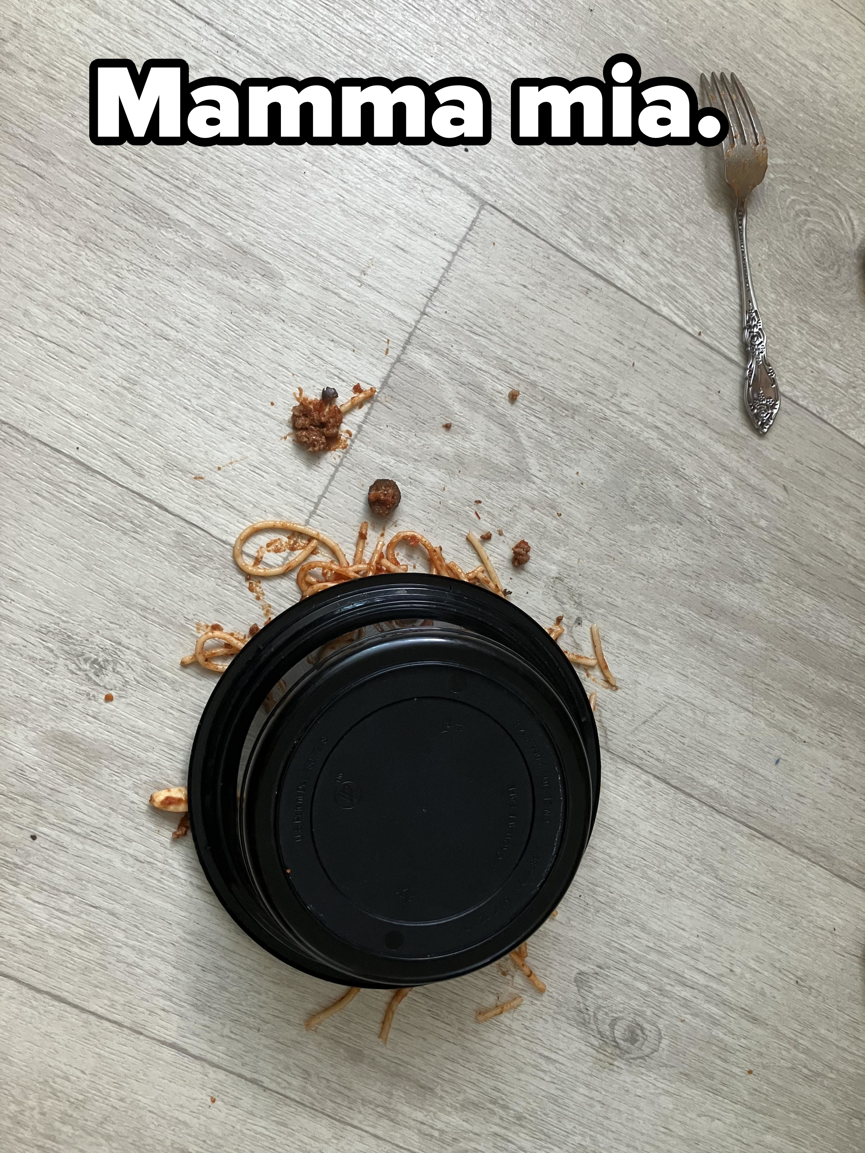 A fallen bowl of spaghetti on a wooden floor, with a fork lying nearby