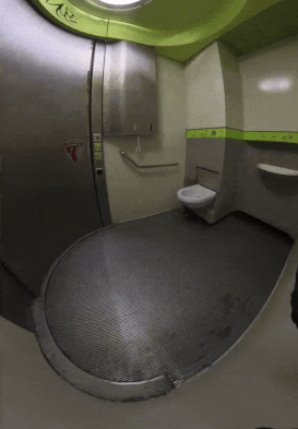 A high-tech airplane bathroom with a retractable automatic door, spacious layout, and a toilet positioned against the wall