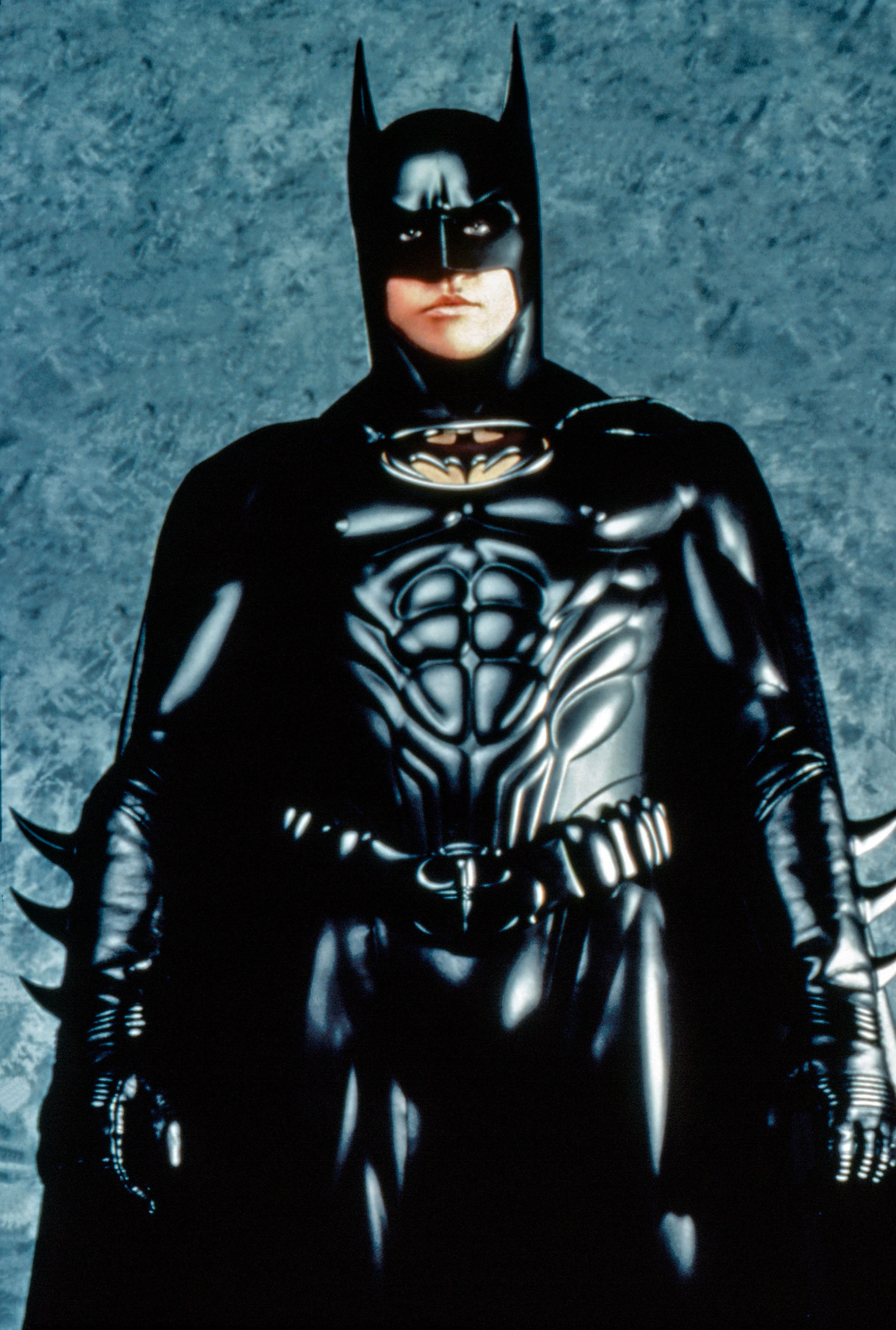 Val Kilmer dressed as Batman in an armored batsuit with a cape and bat-shaped cowl