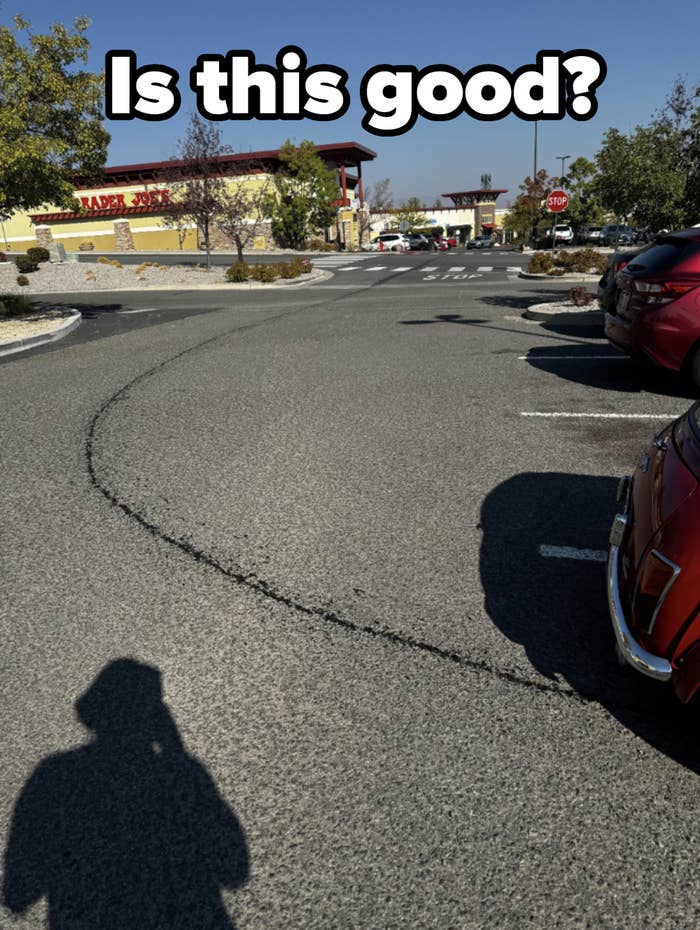 A parking lot with several parked cars and a Trader Joe's store in the background. A person's shadow is seen in the foreground