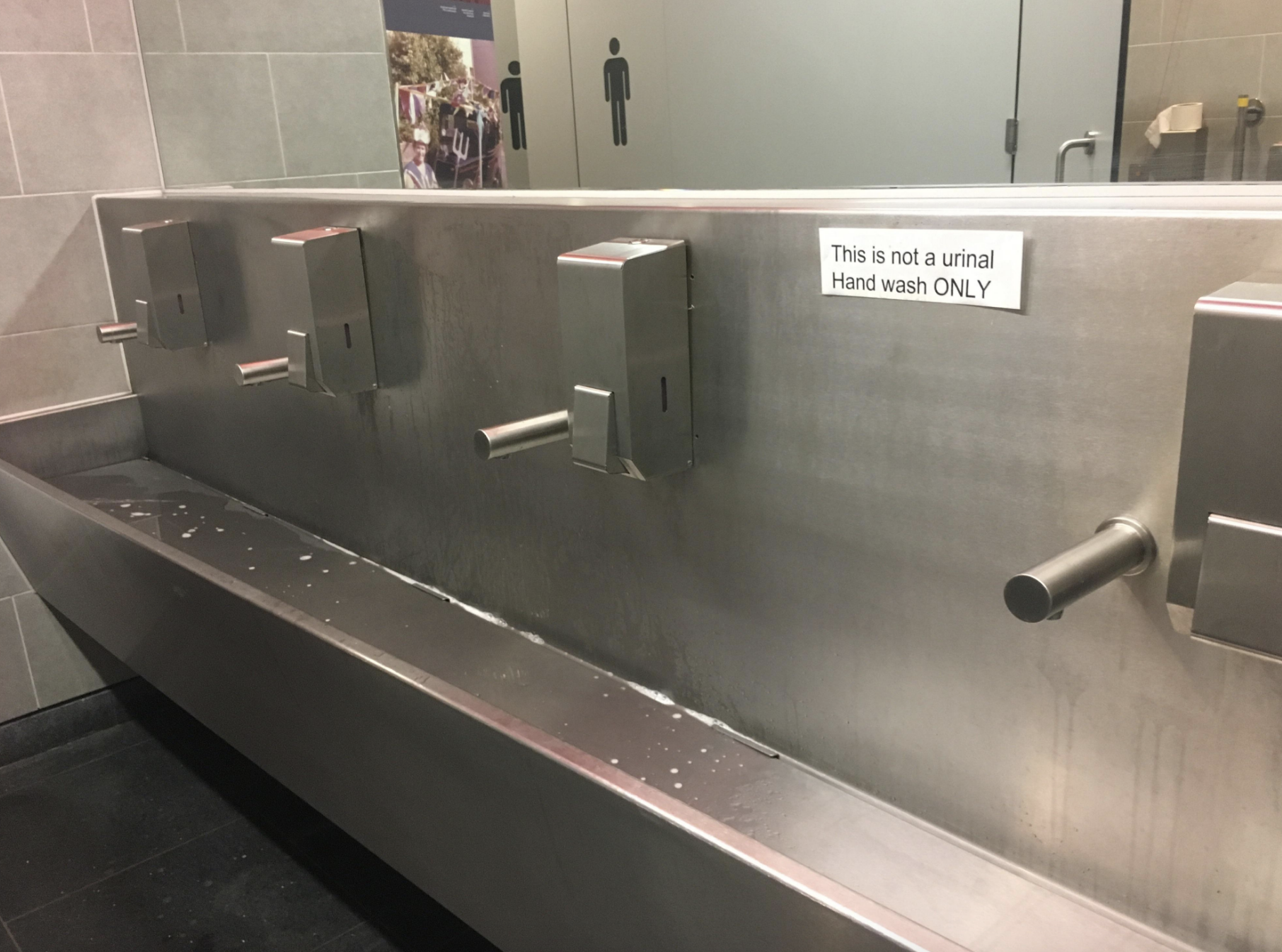 Hand washing station with a sign that reads, "This is not a urinal. Hand wash ONLY." Multiple soap dispensers and faucets are visible above a long sink