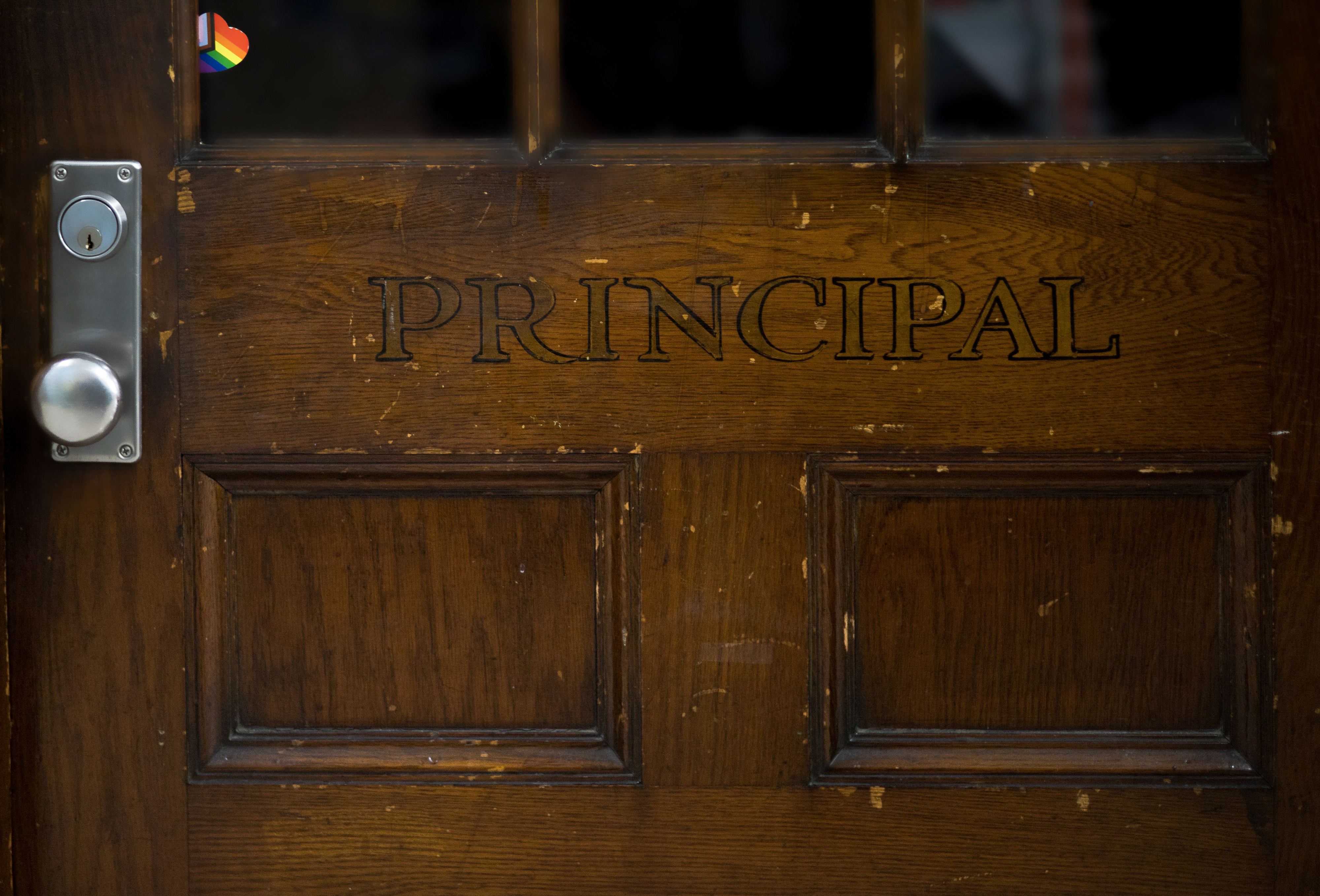 Wooden door with the word &quot;PRINCIPAL&quot; engraved, featuring a small rainbow pride flag sticker near the upper left corner