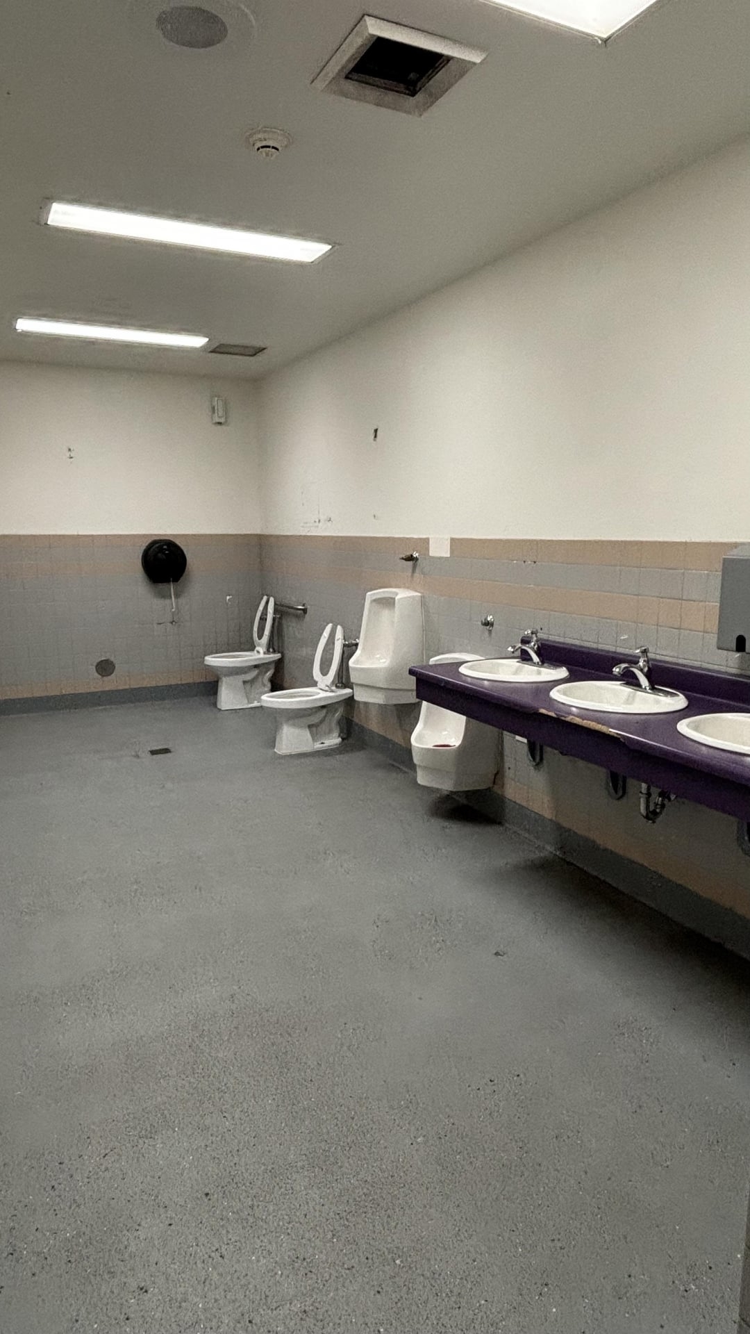 Restroom with three sinks, two toilets, and a urinal, all without dividers or stalls