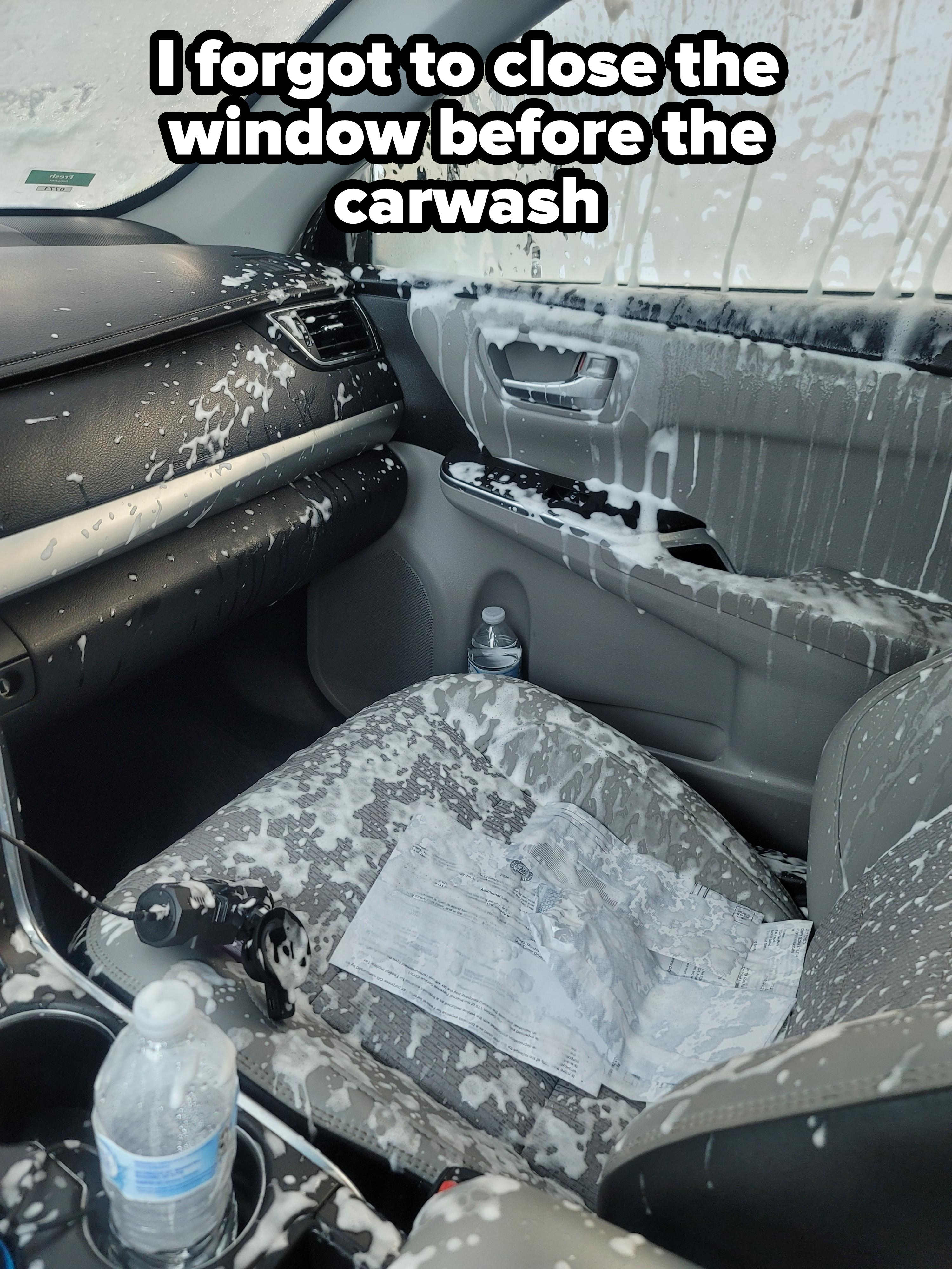 The interior of a car is covered in what appears to be spilled white foam, including the front seat, dashboard, and door. A water bottle and some papers are on the seat