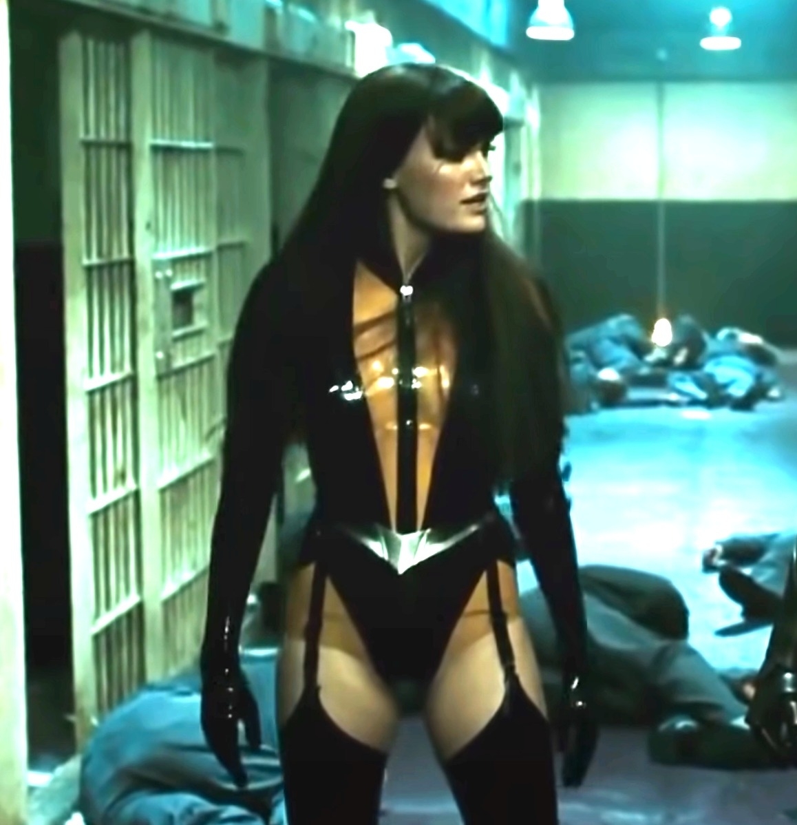Malin Åkerman as Silk Spectre II in "Watchmen," wearing a tight latex suit, standing in a dimly lit hallway with inmates on the floor around her