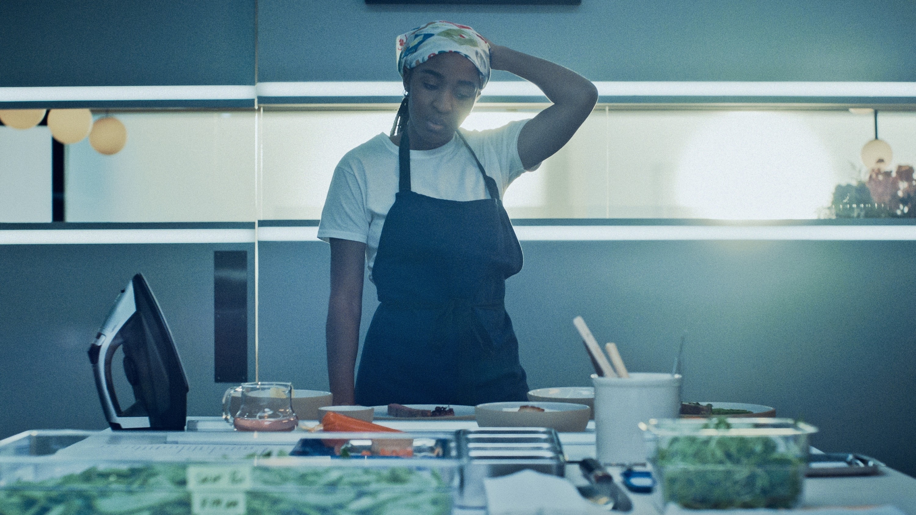 Ayo Edebiri in an apron and white tee while standing in a restaurant kitchen in &quot;The Bear&quot;