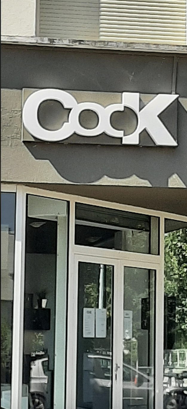 Storefront with the name "Cook" displayed above the entrance. Signs are visible on the door and inside the shop