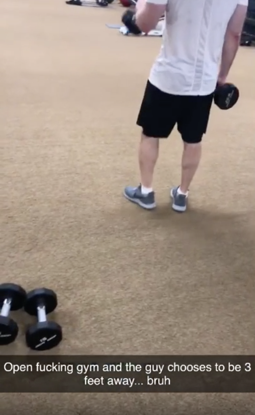 A person in a gym holding a dumbbell, with another dumbbell on the floor. Text reads: "Open fucking gym and the guy chooses to be 3 feet away… bruh"