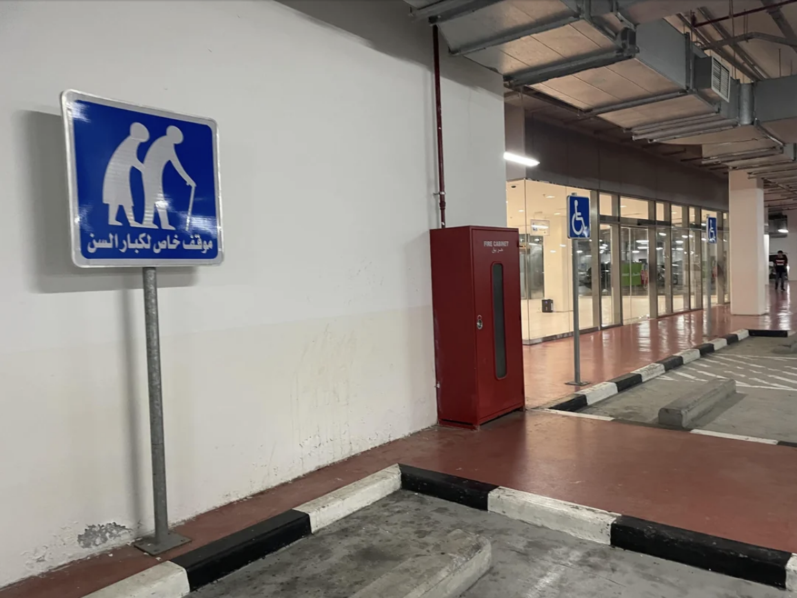 Designated parking area with signs for elderly and disabled individuals in a covered parking facility, near an entrance and a fire extinguisher