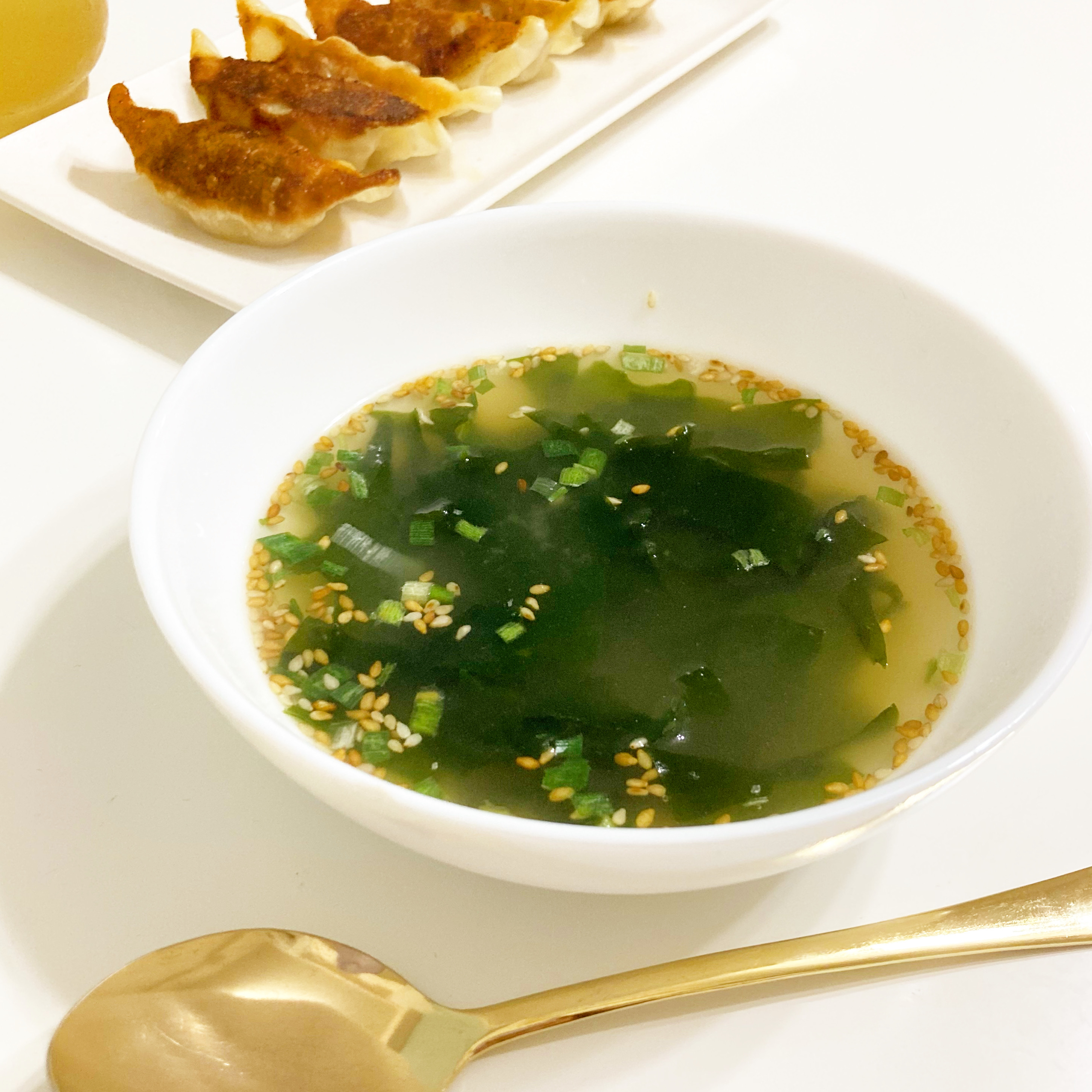 白い器に盛り付けられたわかめスープと餃子数個が並んでいる食卓の様子。