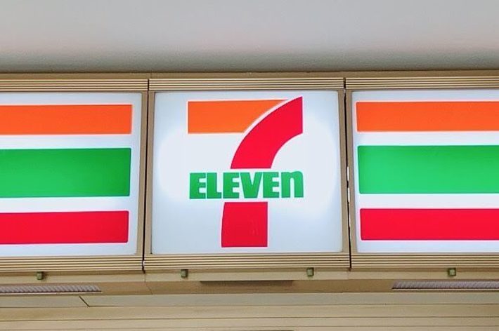 セブンイレブンの入口。上部にお馴染みのロゴと看板が見える。中には商品陳列棚が並んでいる。