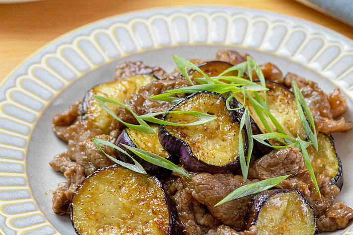 皿に盛り付けられたナスと牛肉の炒め物。ネギが添えられている。