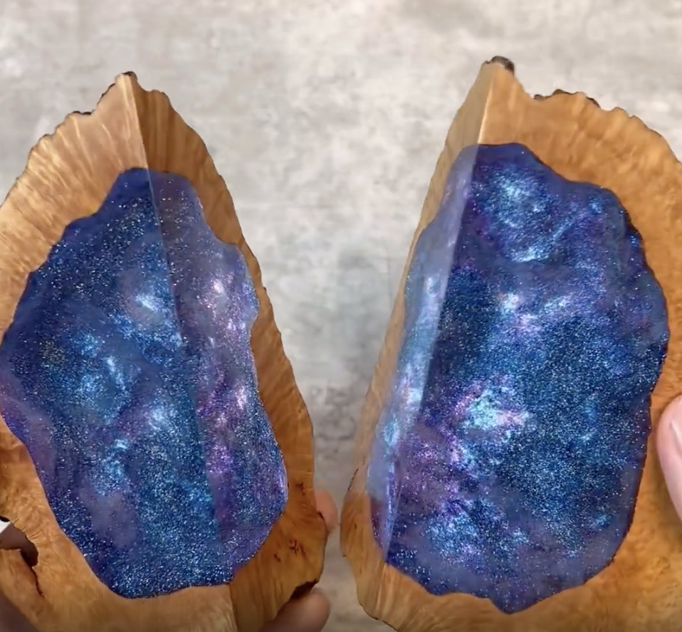 "A pair of hands holding two wooden pieces split open to reveal a shimmering, galaxy-themed resin center."