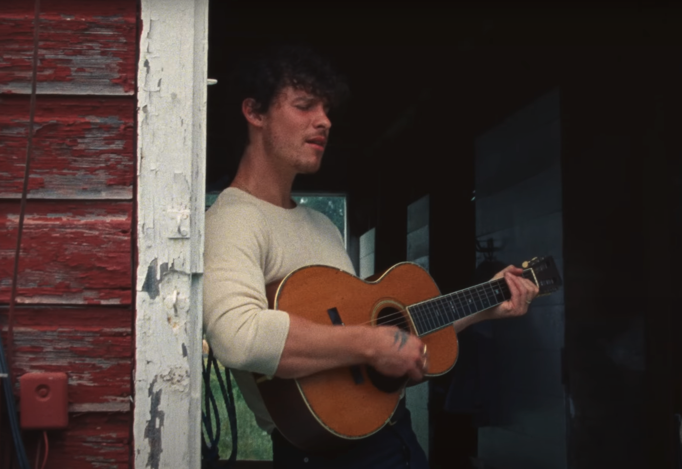 Shawn Mendes playing acoustic guitar on a porch
