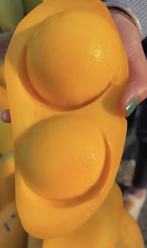 Hand holding a uniquely shaped, yellow fruit resembling a large mango with two round bulges on one side