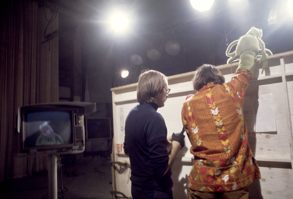 Jim Henson and Frank Oz operate Kermit the Frog on a set, Kermit visible on a TV monitor