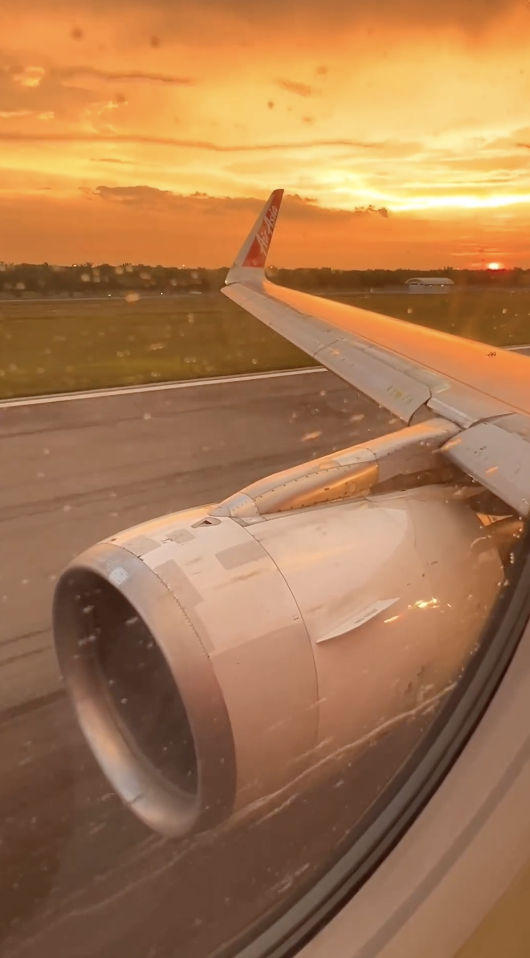 View from an airplane window showing the aircraft's wing and engine during takeoff, with a scenic sunset in the background
