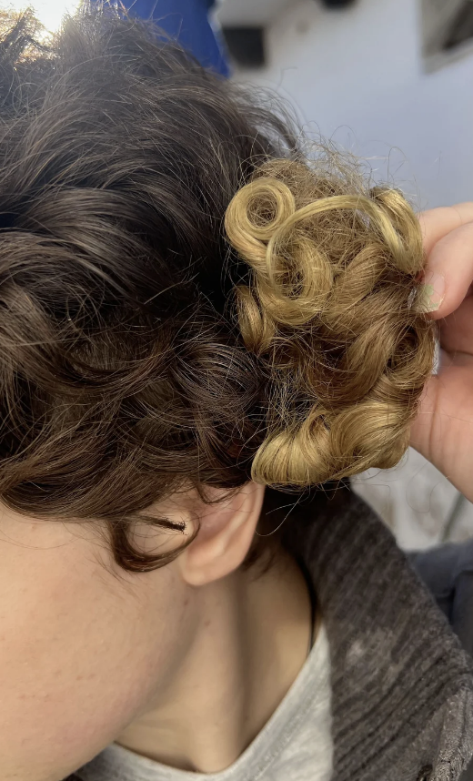 Person's hand showing a section of their curly hair, with lighter curls highlighted among darker curls