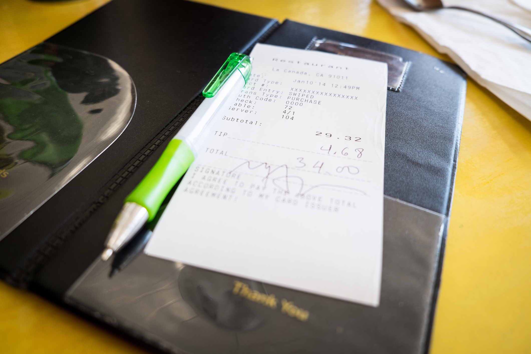 A restaurant receipt with a total amount of $34.00, a pen, and a holder that says "Thank You."