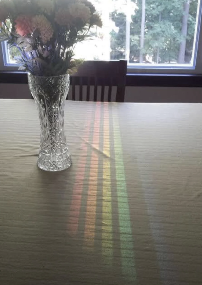 A vase with flowers on a table with a rainbow reflection from the window creates a colorful pattern on the tablecloth