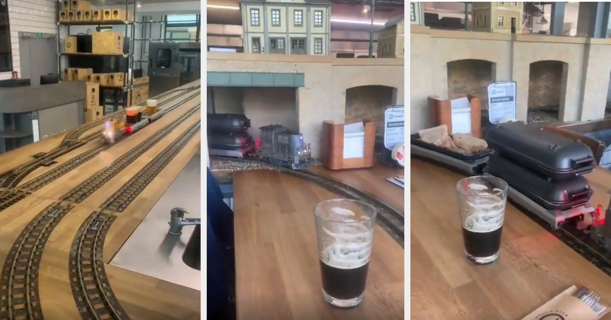 Model trains transporting drinks along tracks in a bar with a pint of dark beer visible on the counter