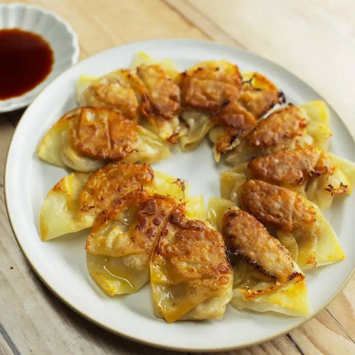 丸い白い皿に盛られた焼きギョーザ。その横にタレの入った小さな皿が置かれています。