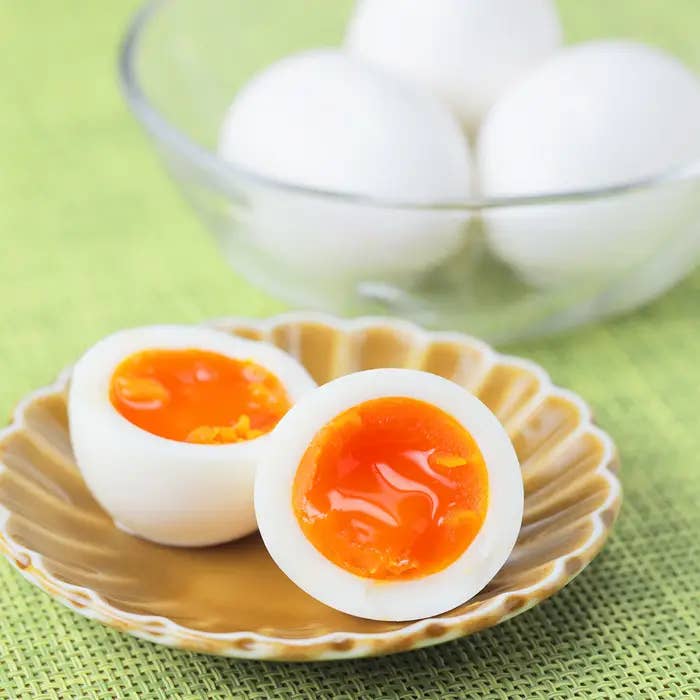 半分に切った半熟卵が皿に盛られている。背景にはガラスボウルに入った白い卵。