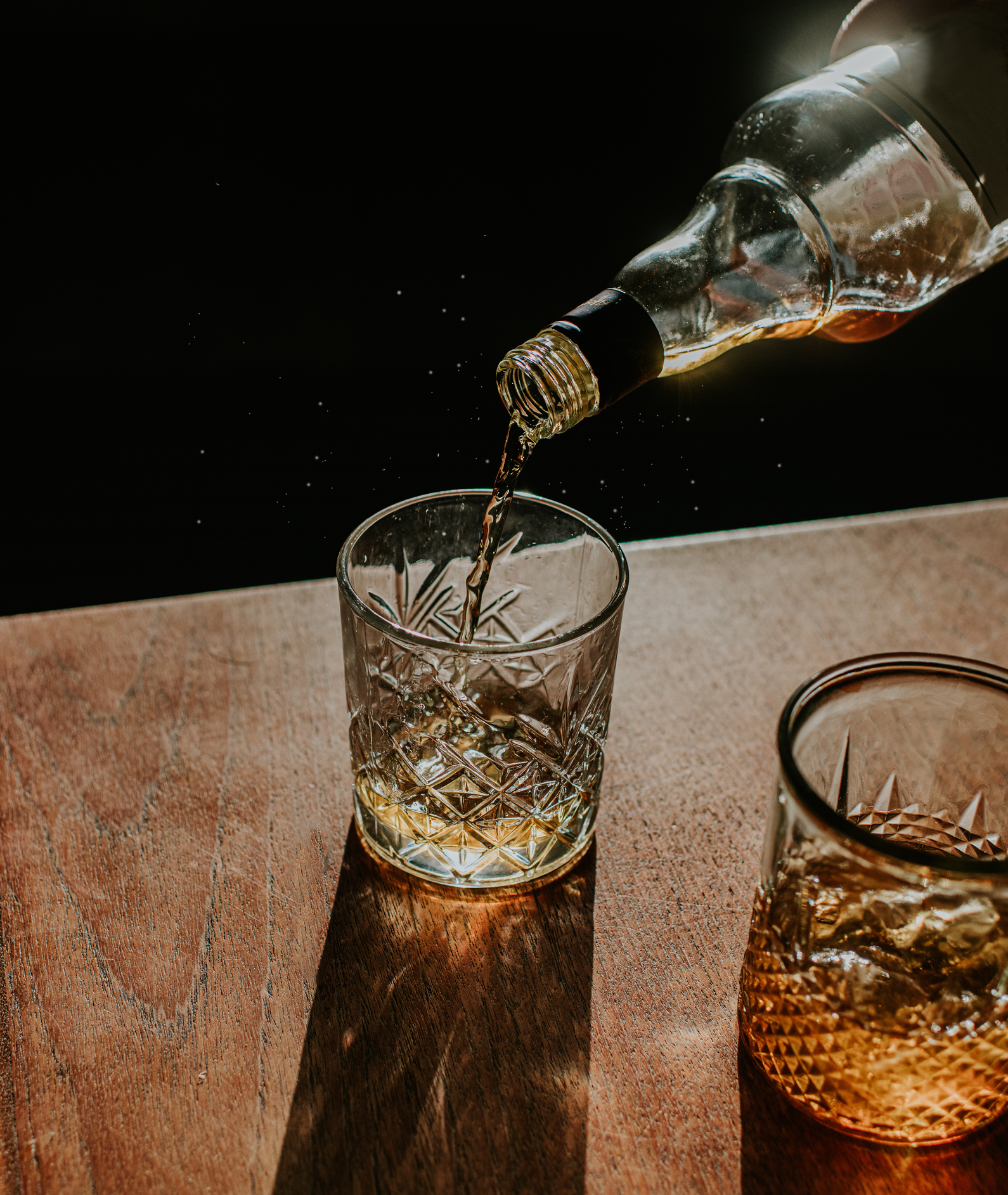 Whiskey being poured into two etched glasses on a wooden table
