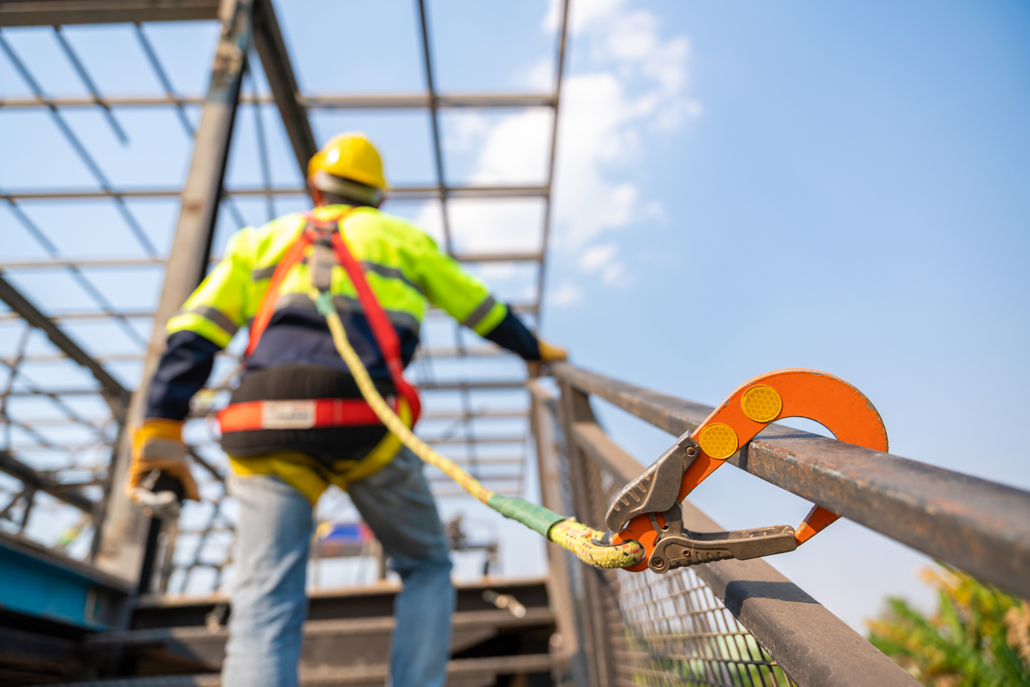 A construction worker wearing safety gear is secured with a safety harness and lanyard while working on a building framework