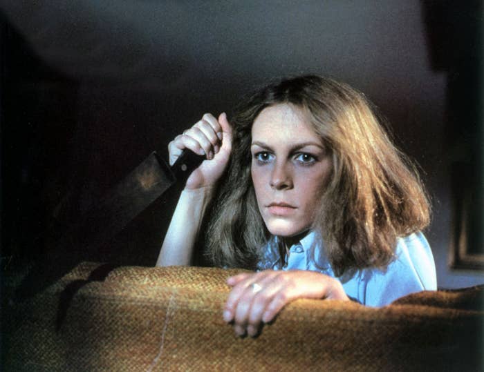 Jamie Lee Curtis holding a kitchen knife while sitting on a brown couch in "Halloween"