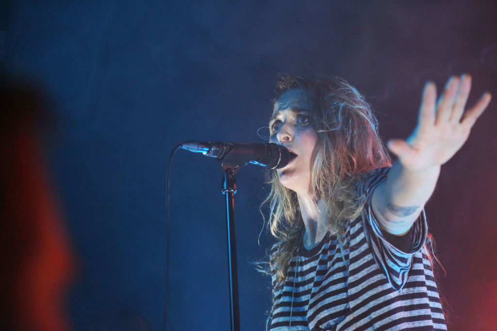 A woman singer in a striped shirt passionately performs into a microphone, extending her hand towards the audience