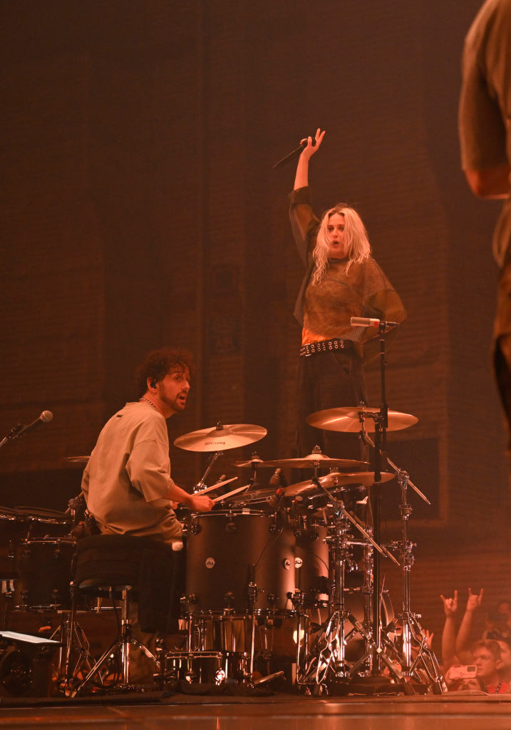 Josh Dun playing drums, Tyler Joseph standing on drum set with microphone during Twenty One Pilots concert performance