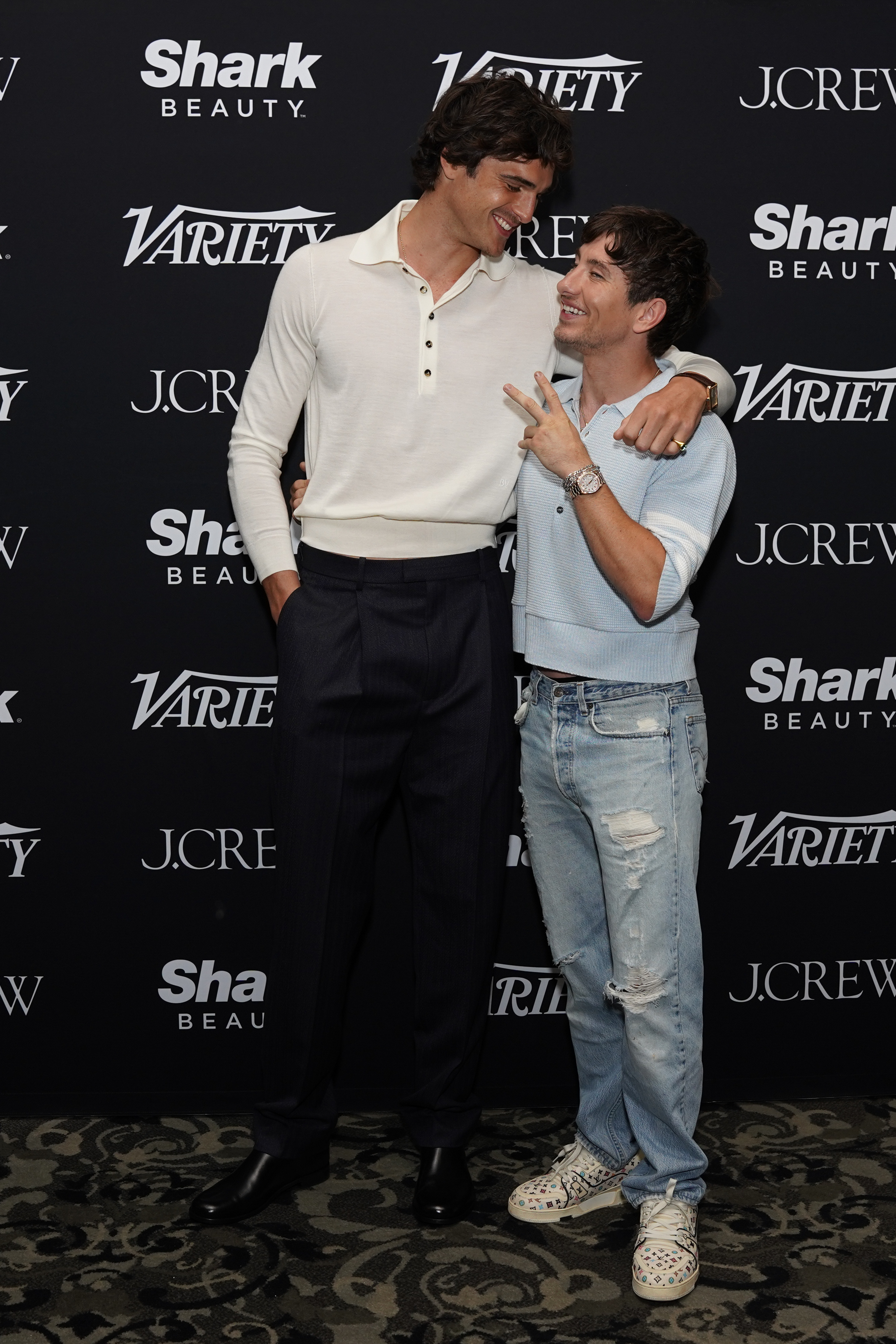 Celebrity event backdrop: Jacob Elordi in a casual shirt and pants, and Kieran Culkin in a light sweater and jeans, smiling and posing together