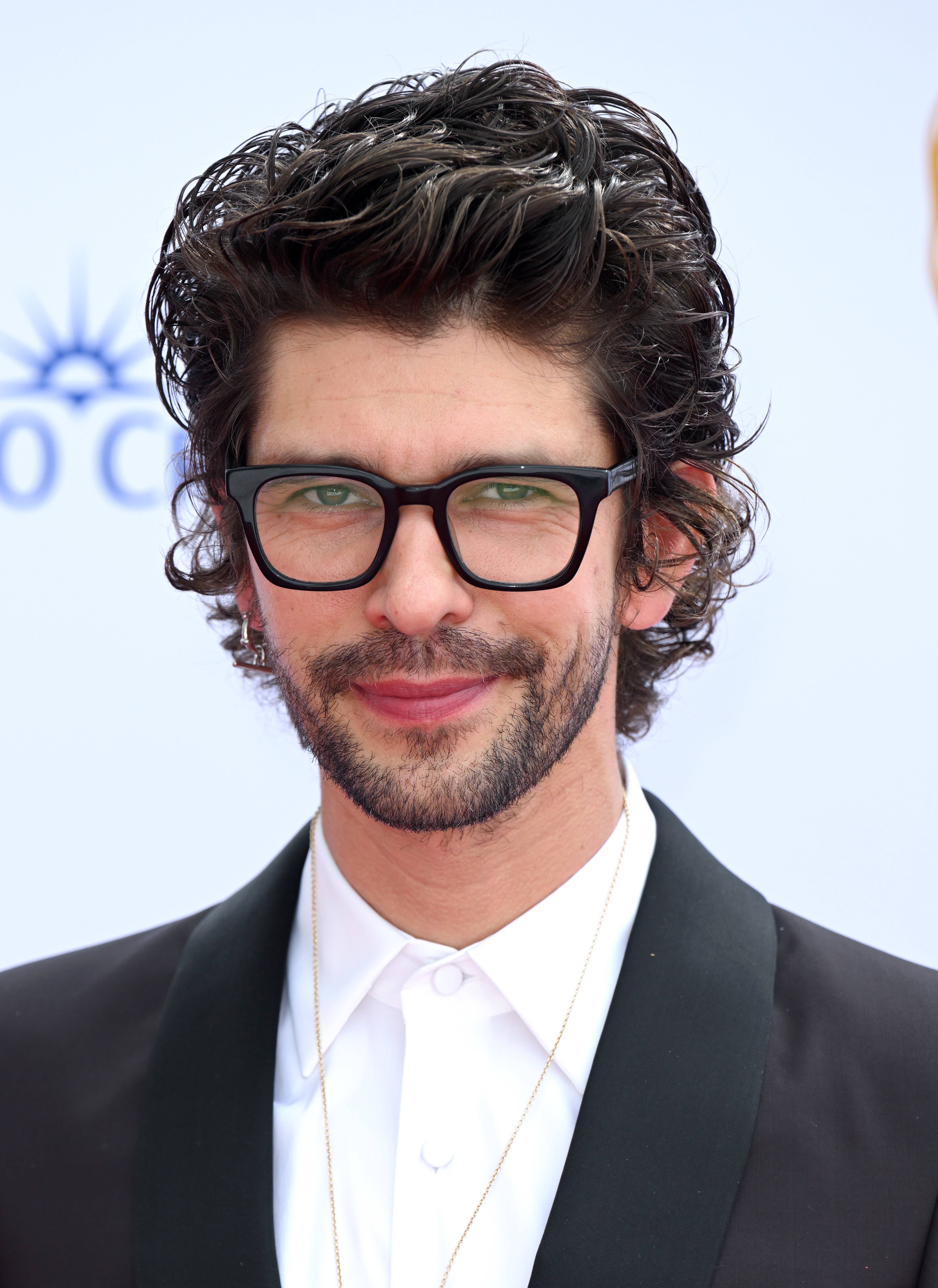 Ben Whishaw at a formal event, wearing a black blazer over a white shirt, sporting glasses and a trimmed beard