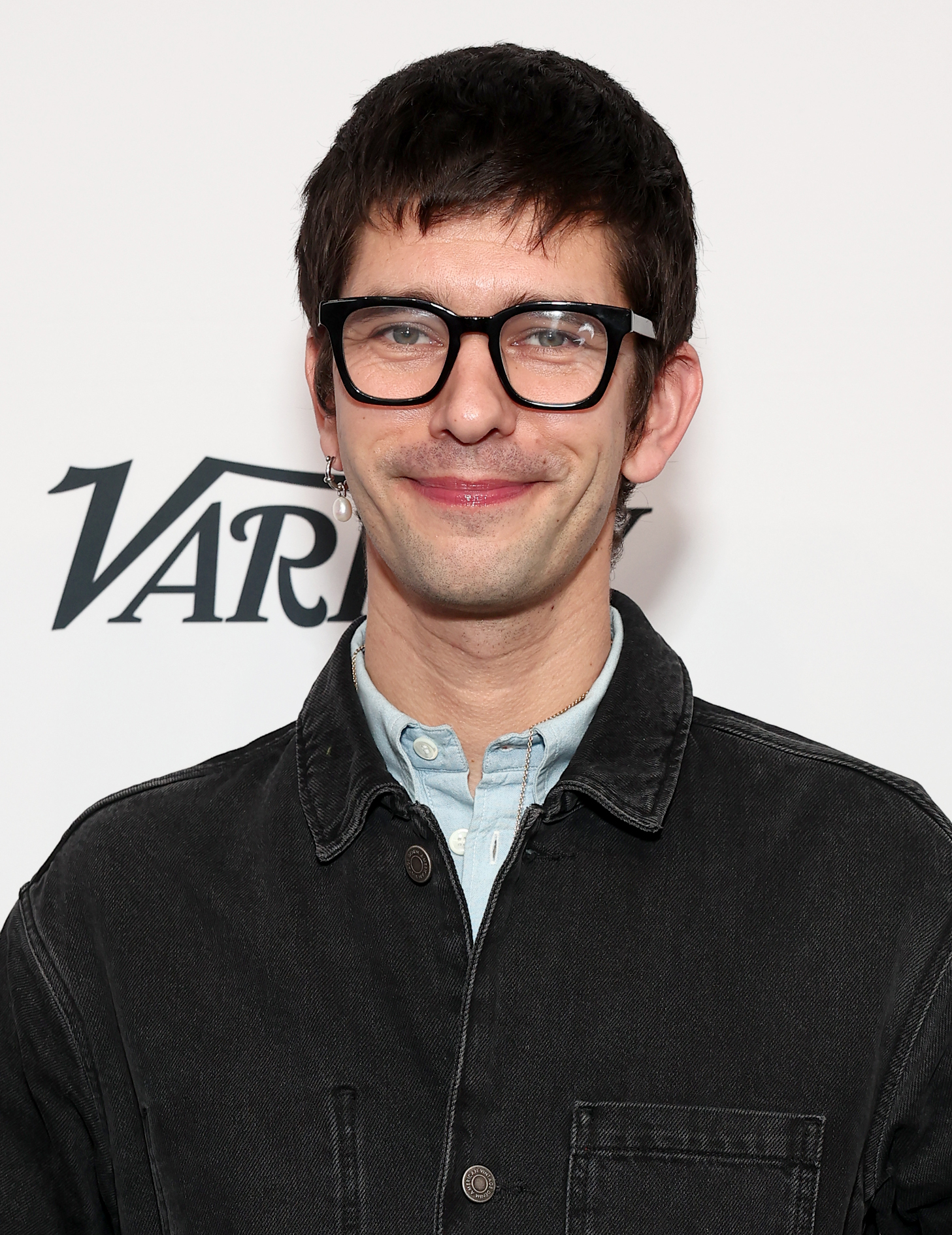 Ben Whishaw, wearing glasses and a denim jacket, smiles at a Variety event