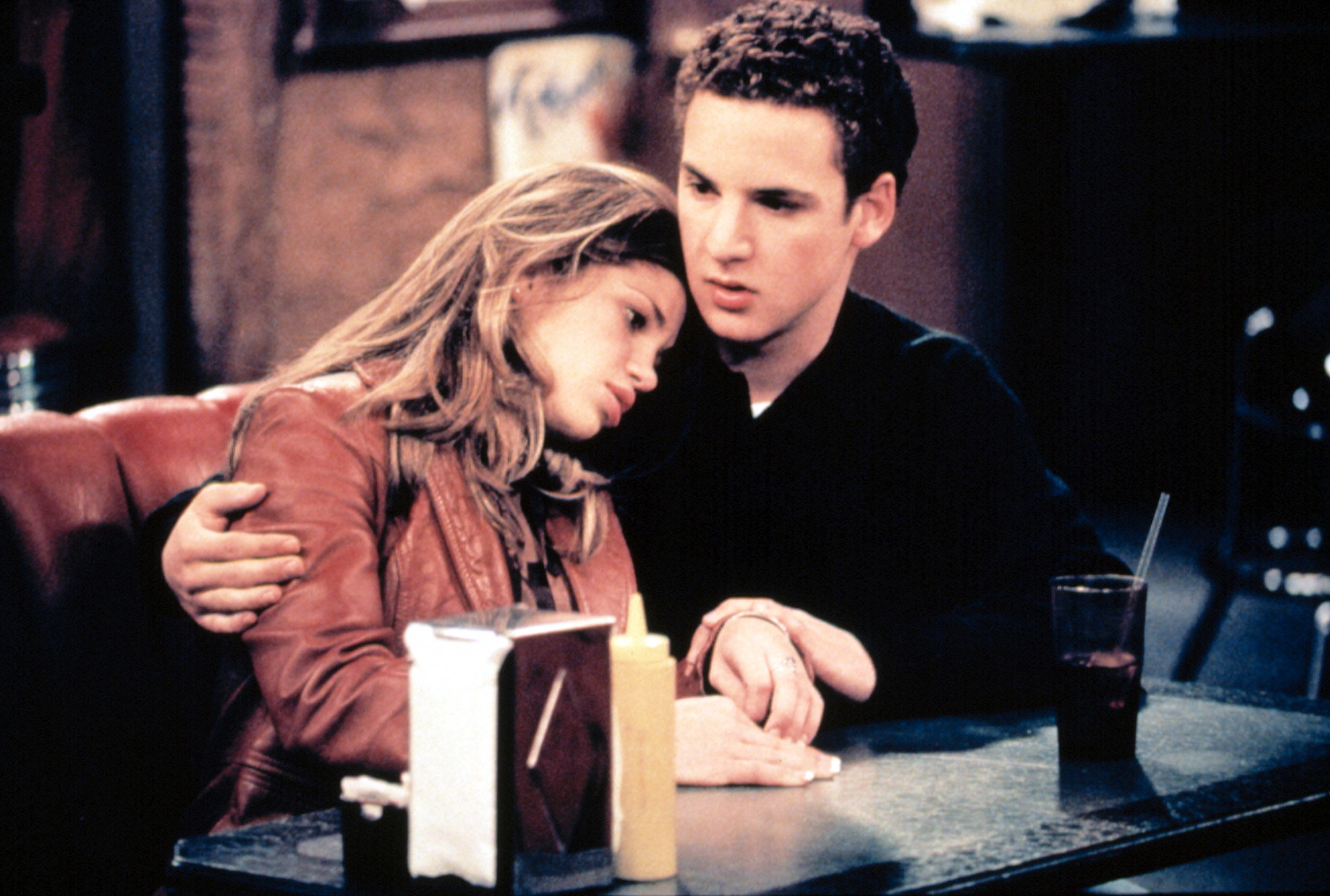 Danielle Fishel and Ben Savage sitting at a restaurant booth looking somber in "Boy Meets World"