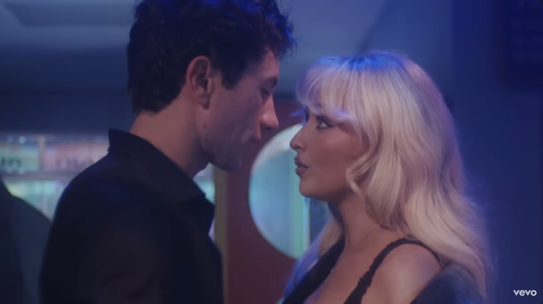 Man and woman stand closely and face each other in a dimly lit room