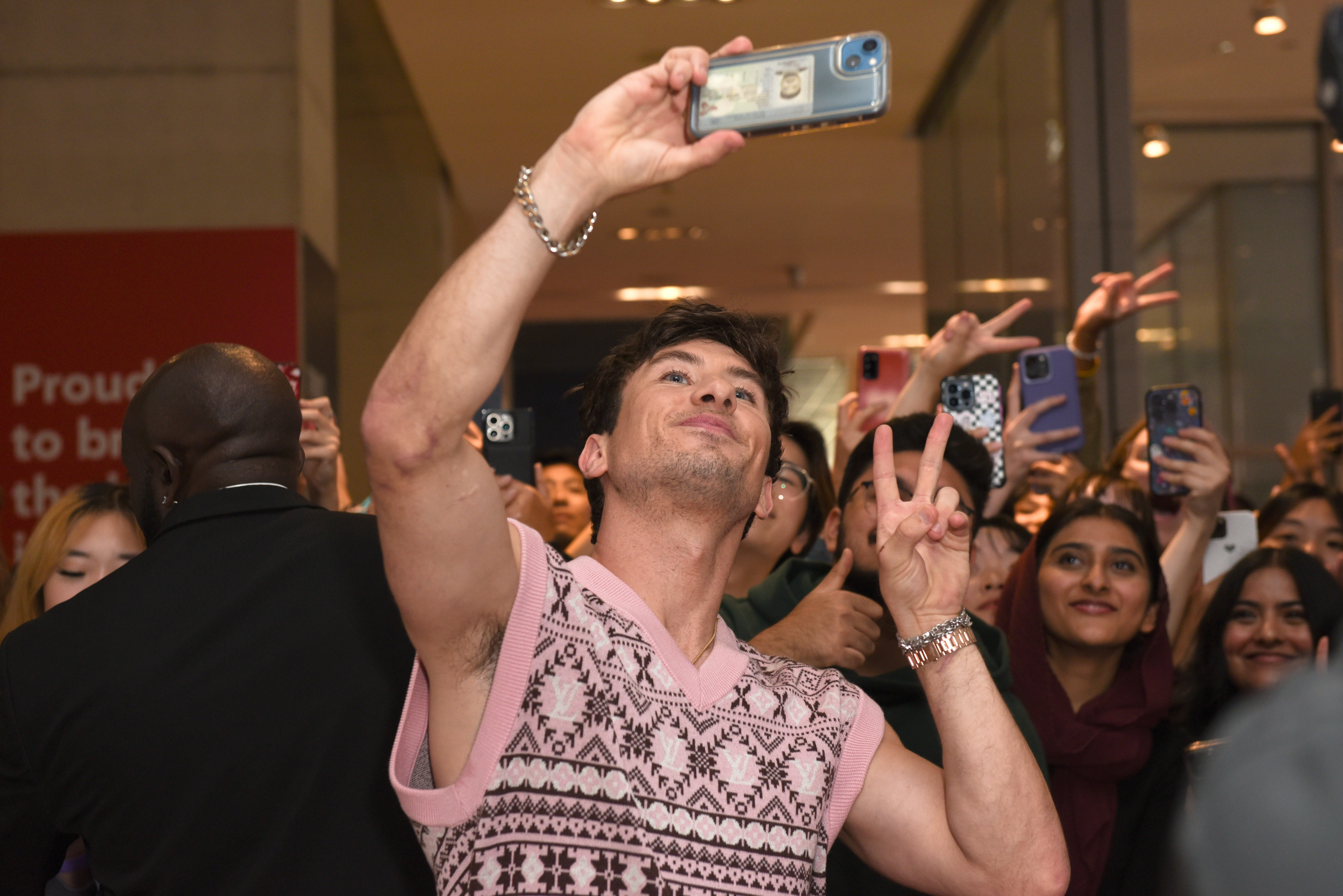 Man taking a selfie while flashing a peace sign. Smiling fans in the background hold up their phones to take pictures