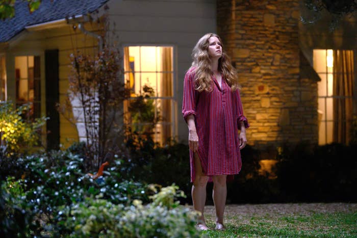 Amy Adams stands barefoot outside a house at night, wearing a loose, knee-length dress, looking concerned