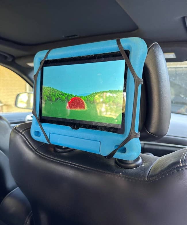 Tablet with a bluish lawsuit mounted to a car headrest, displaying a colorful animated country with a reddish entity and greenish trees