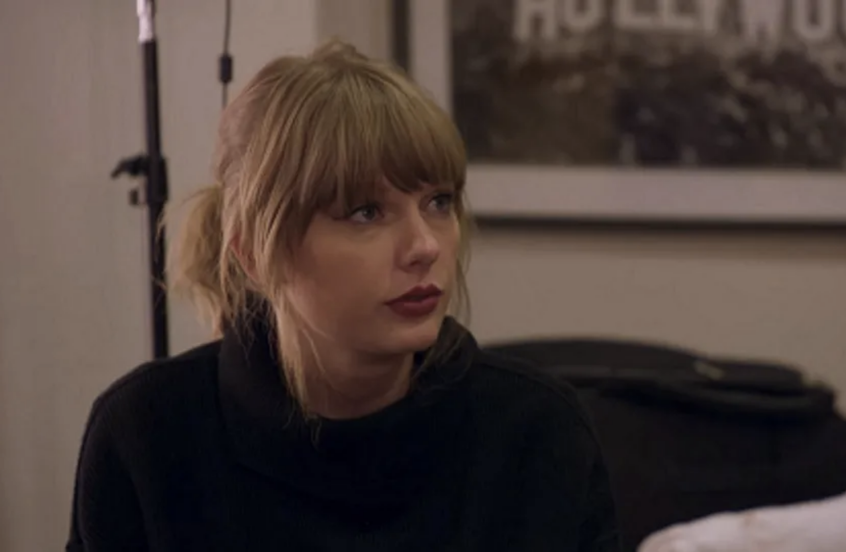 Taylor Swift in a casual setting with a serious expression, wearing a dark, minimalistic outfit