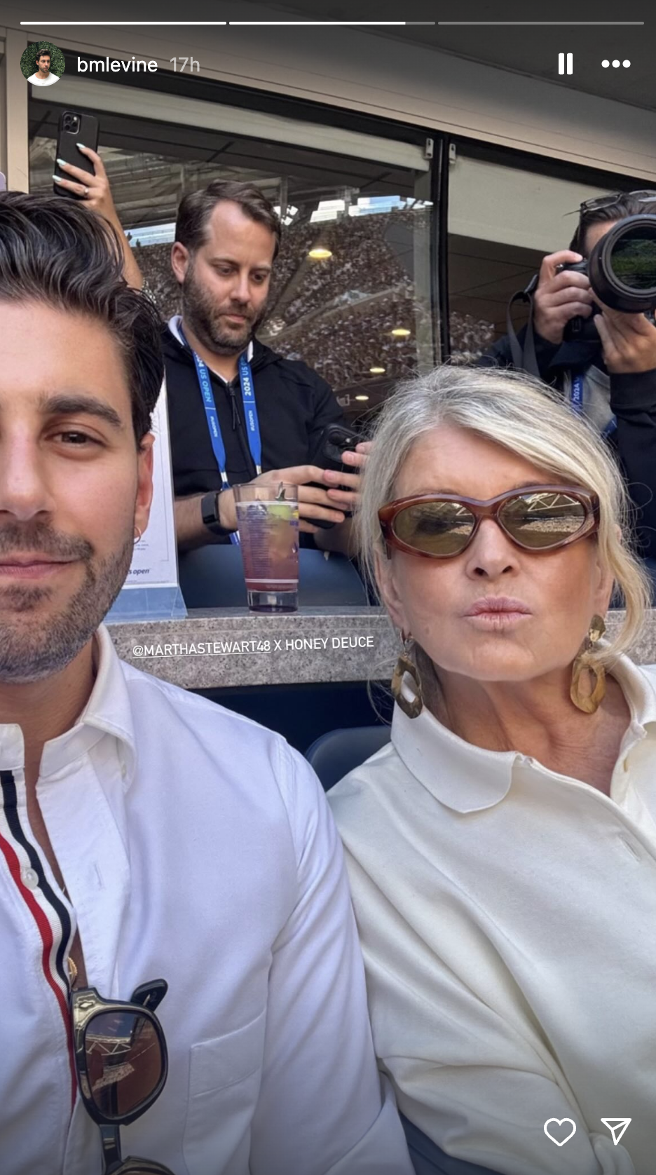Ben Levine and Martha Stewart pose for a selfie at a stadium. Martha Stewart wears sunglasses and a white shirt. Ben Levine also wears a white shirt