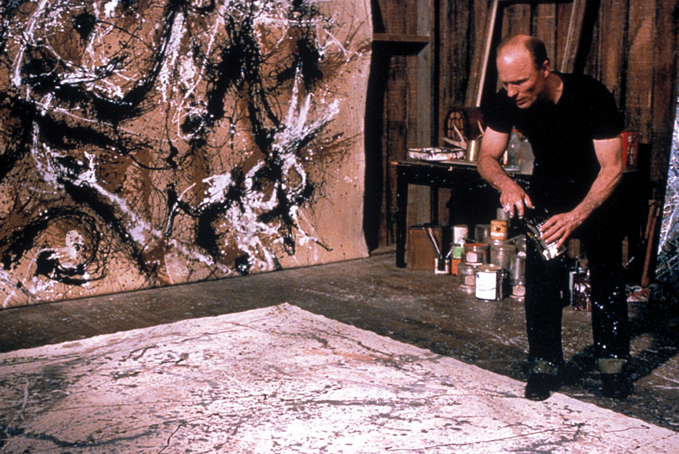 Ed Harris, dressed in casual clothing, is seen creating a large splatter painting in this scene from the movie &quot;Pollock&quot;